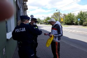 Osoba otrzymuje maseczkę ochroną od policjanta i strażnika miejskiego