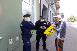 Osoba otrzymuje maseczkę ochroną od policjanta i strażnika miejskiego